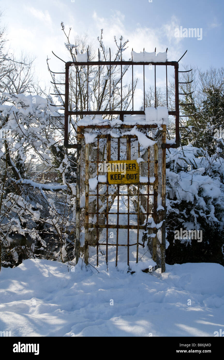 Danger Keep Out reads the sign on a locked metal gate leading across a bridge to an electricity sub station Stock Photo