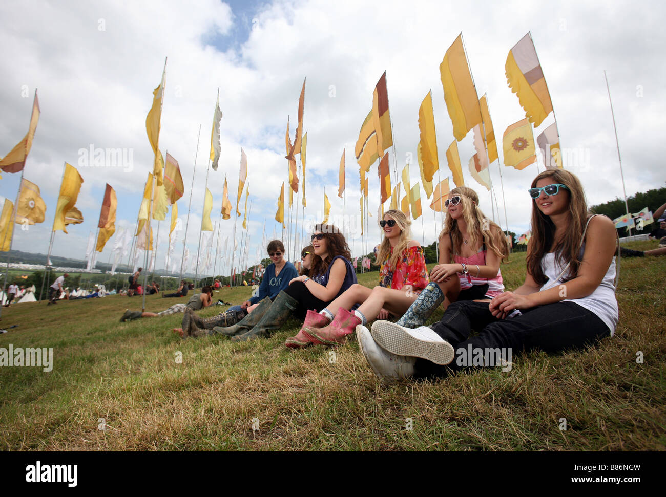 A group of girls enjoy the sunshine sat among flags at the Glastonbury Festival in Pilton, Somerset in the UK. Stock Photo