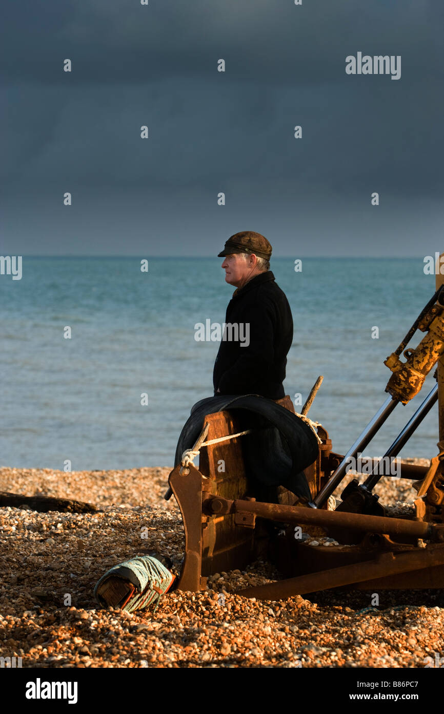 A man seated on heavy machinery a tracked vehicle on the shingle beach and shoreline at Dungeness in Kent, UK. Stock Photo