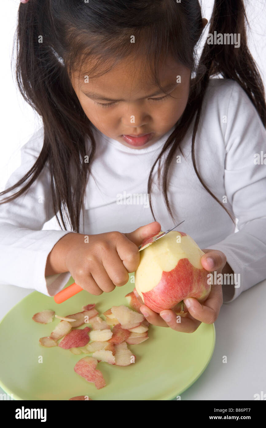 Little girl is peels an apple with a knife Stock Photo