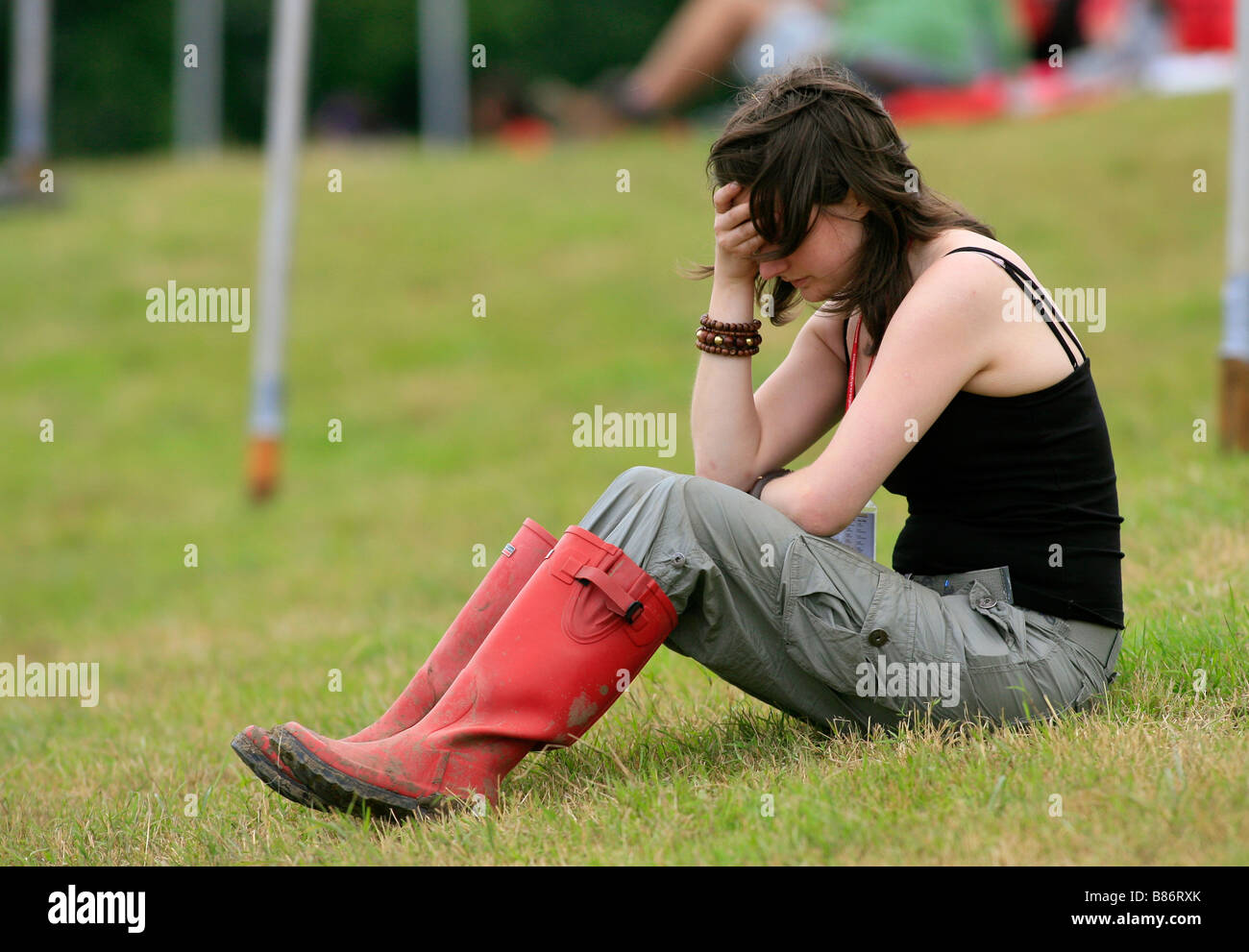 A girl in wellies holds her head after a heavy night out at the Glastonbury festival in Pilton, Somerset in the UK. Stock Photo