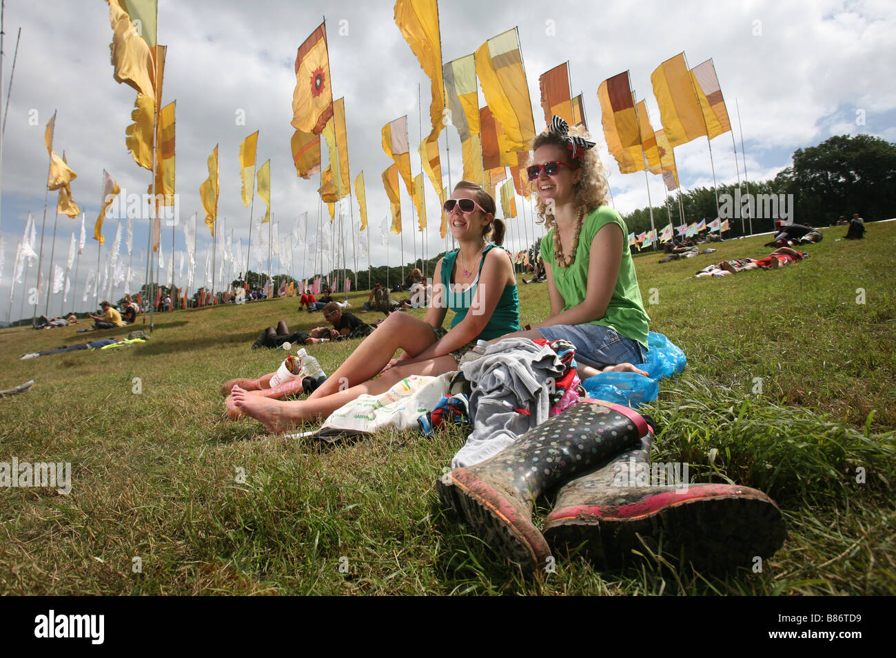A pair of girls enjoy the sunshine sat among flags at the Glastonbury Festival in Pilton, Somerset in the UK. Stock Photo