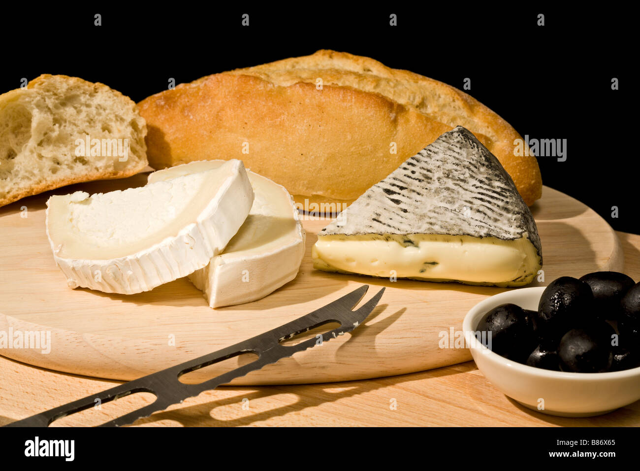 blue mould cheese and goat cheese with white bread and black olives on wooden platter Stock Photo