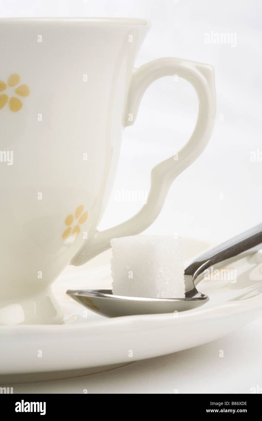 A sugar cube on a tea spoon on the saucer of a tea cup Stock Photo