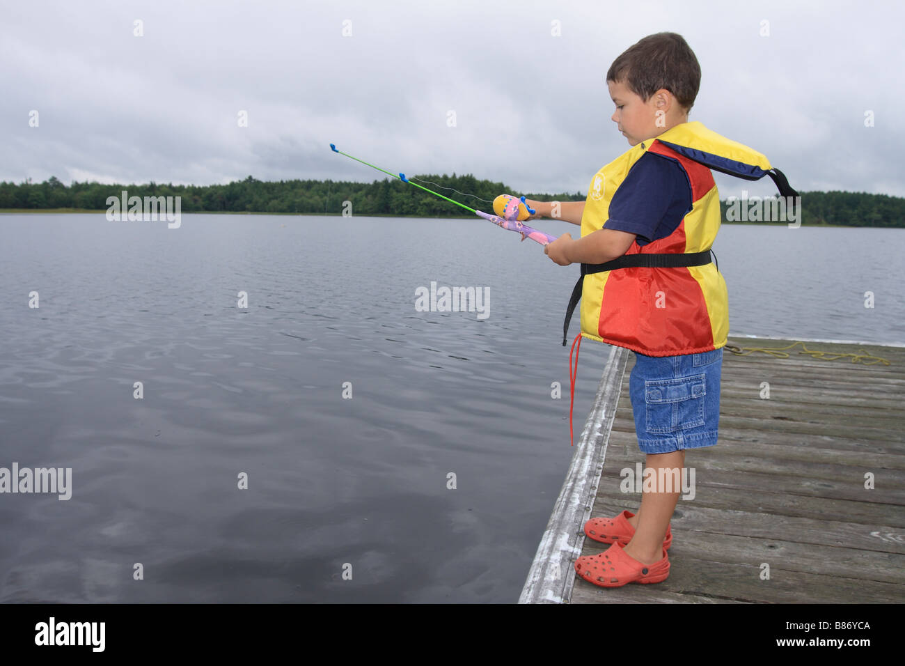 4 year old child wearing a life jacket standing on a wharf using a fishing  rod Stock Photo - Alamy