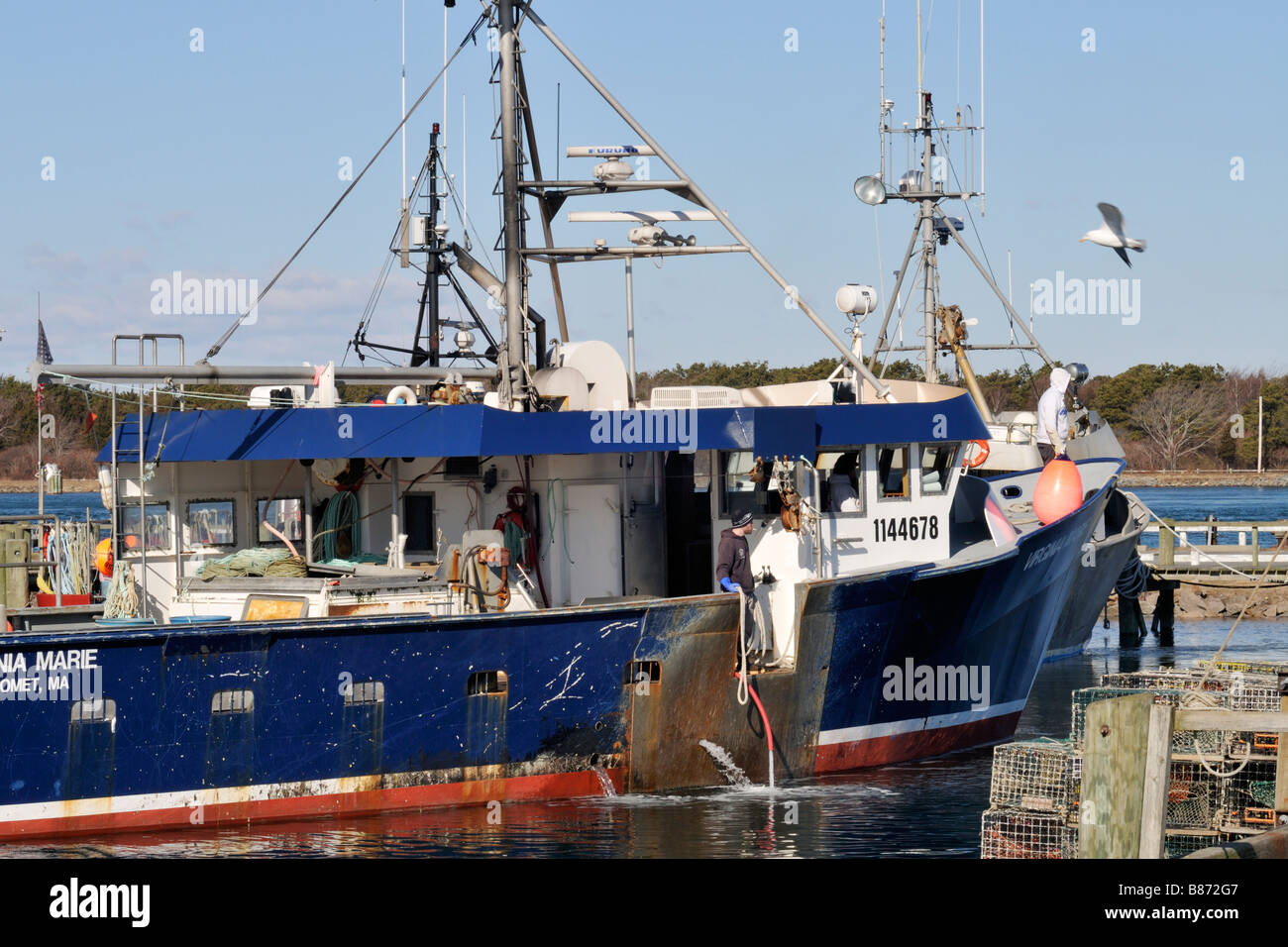 Blue hull fishing boat preparing to dock at pier with fishermen manning