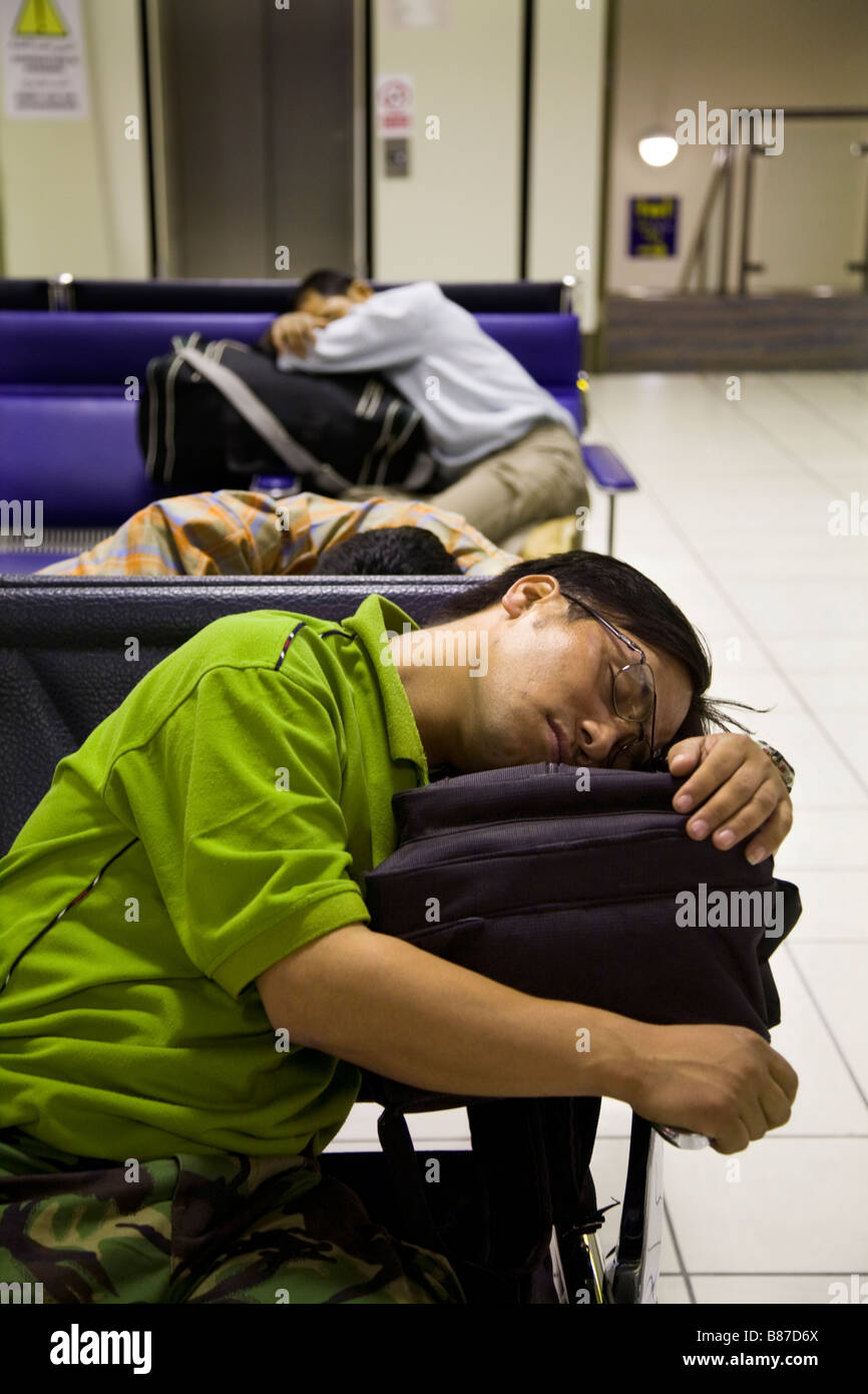 Young men sleep on chairs in the departure lounge of Bahrain international airport, while