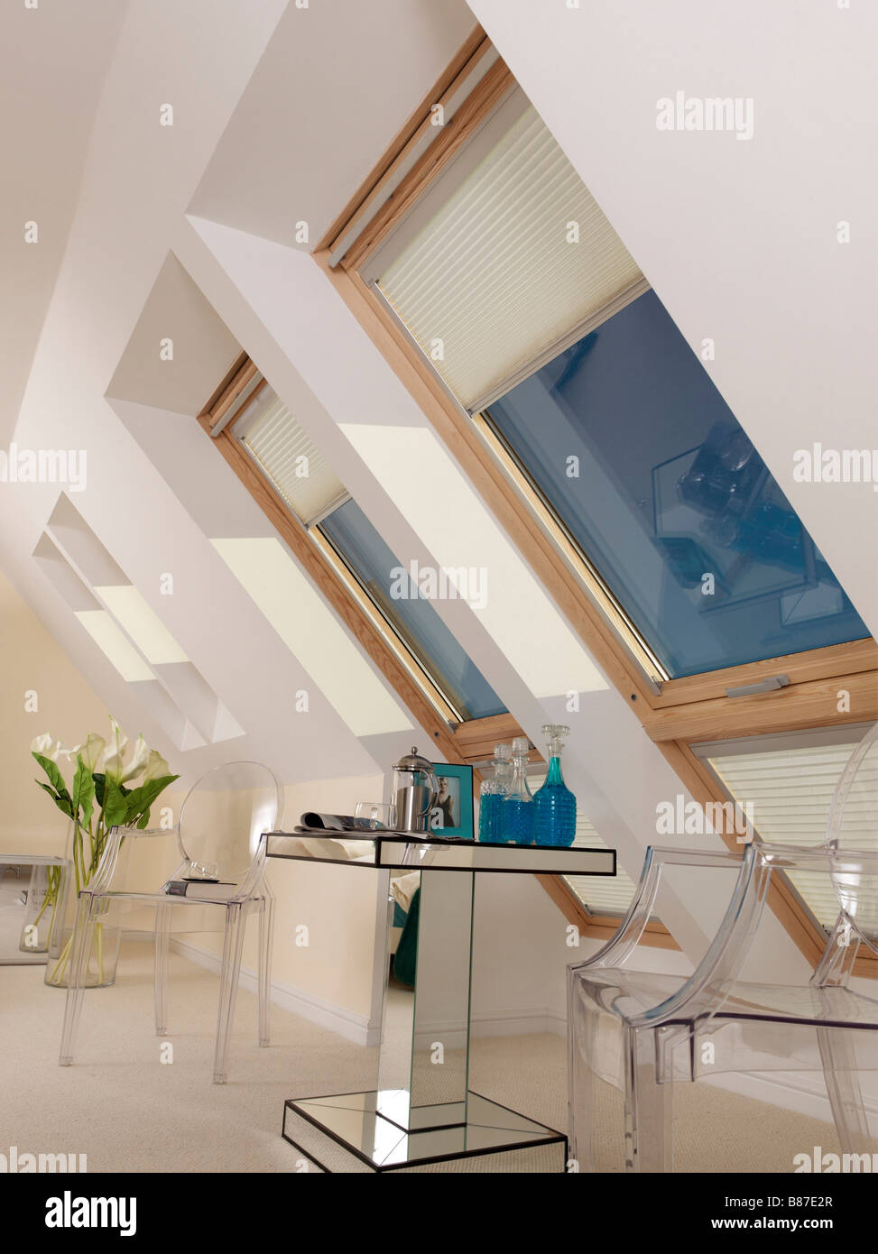 large velux window with blind and blue sky with table and chairs and large vase of flowers Stock Photo