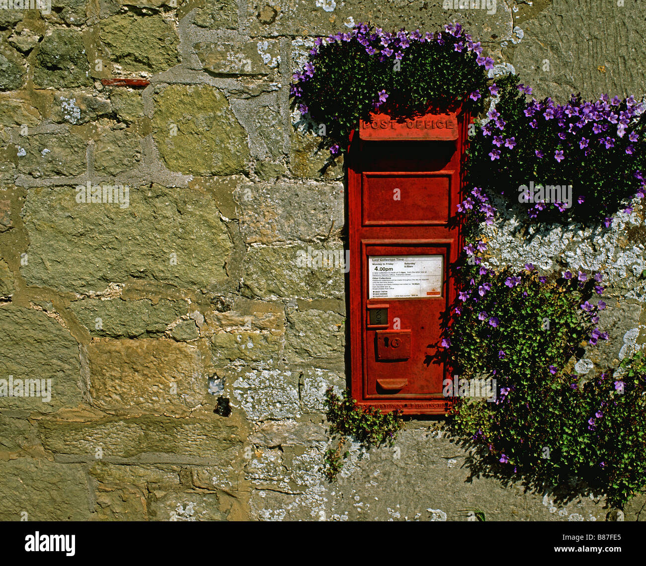A post box in a old stone wall with flowers growing around it Stock Photo