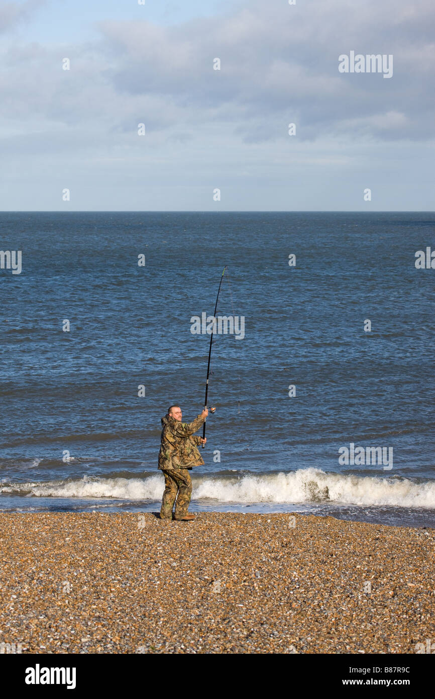 Sea angler fisherman casting rod into sea at Cley shingle bank Stock Photo