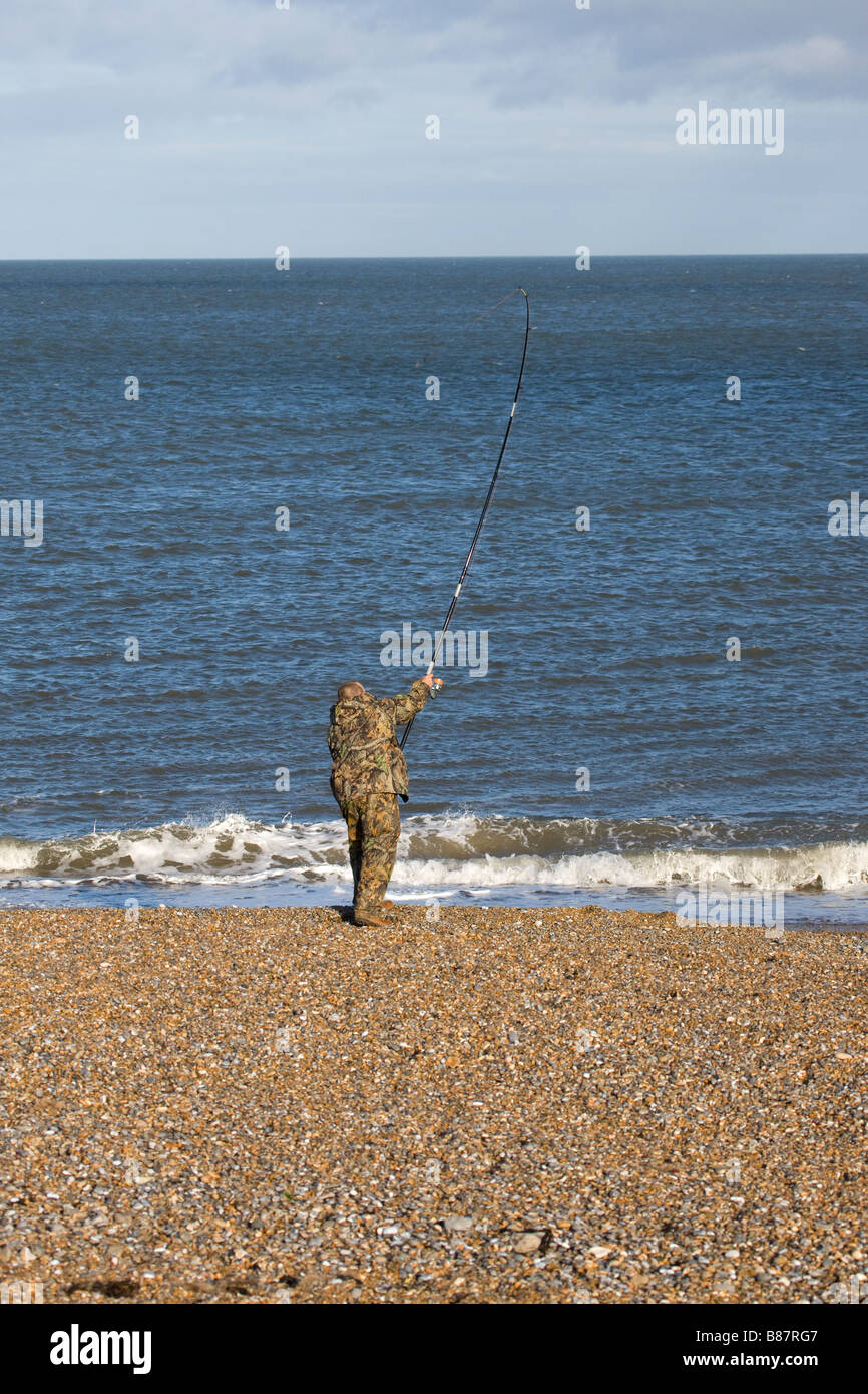 Sea angler fisherman casting rod into sea at Cley shingle bank Stock Photo