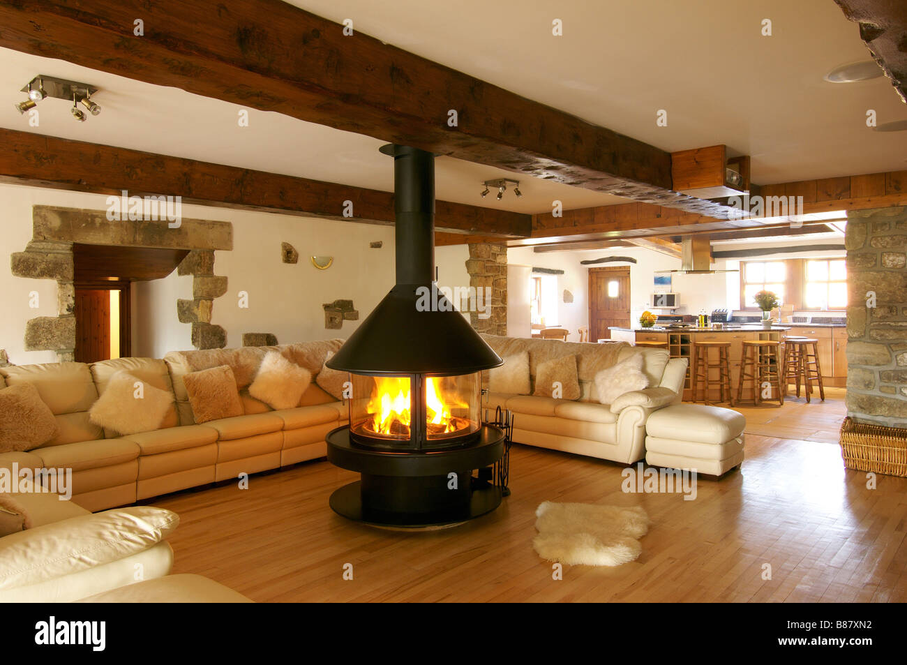 living room with large corner sofa and central fireplace with lit fire and  views through to kitchen Stock Photo - Alamy