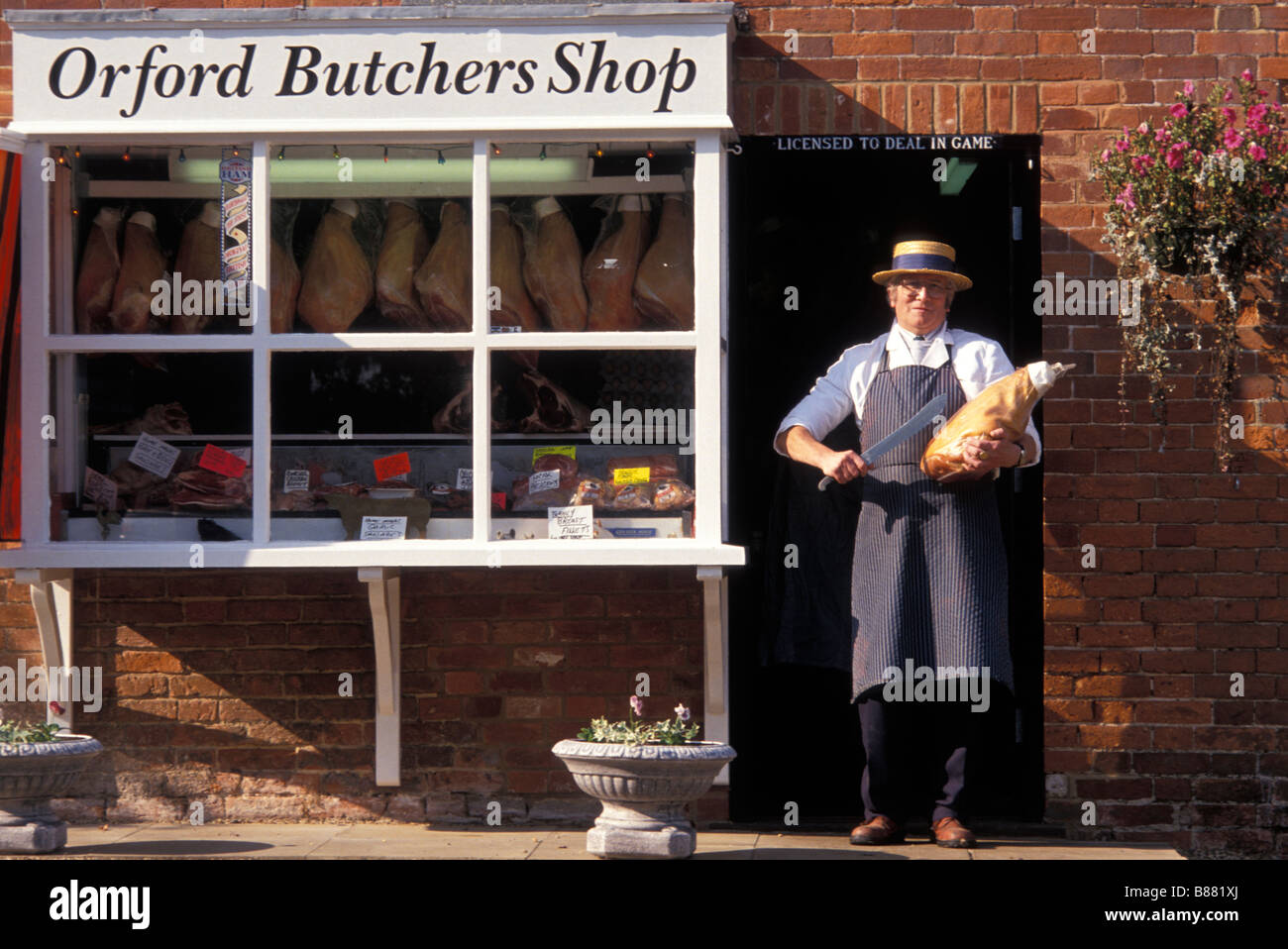 A traditional butcher proudly displays a cut of meat in the doorway of his local butchers shop. Orford Woodbridge Suffolk UK Stock Photo