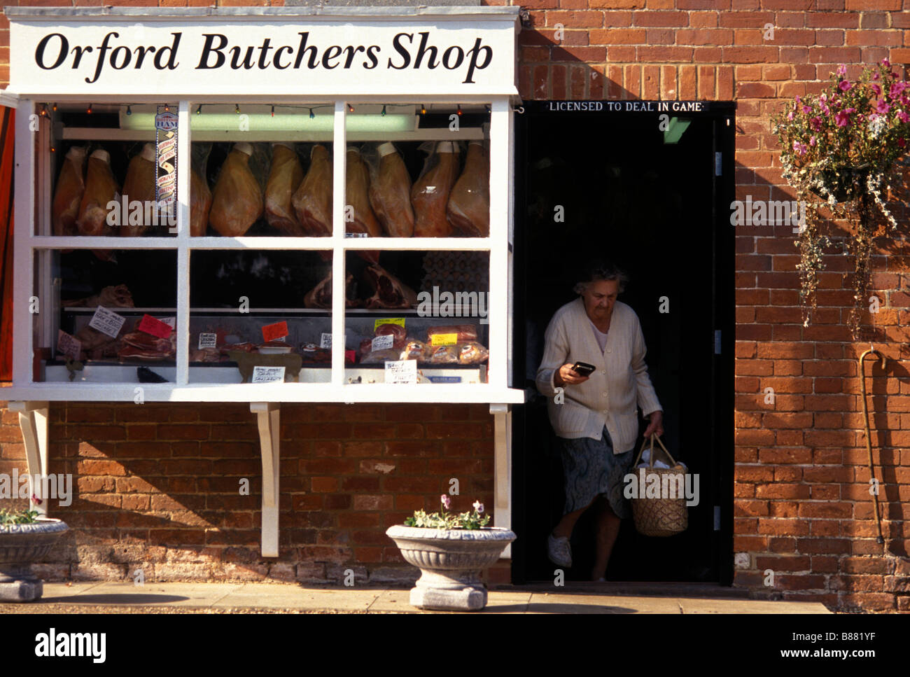 A woman carrying a shopping basket leaves a traditional local butchers shop in Orford. Woodbridge Suffolk England UK Stock Photo