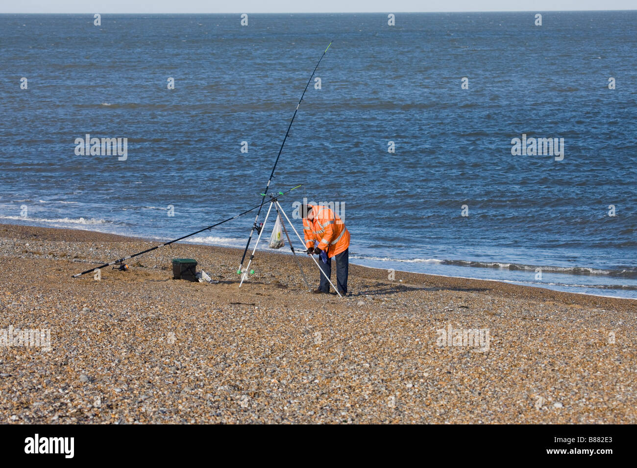 Sea angler fisherman attending to his rods at Cley shingle bank Stock Photo