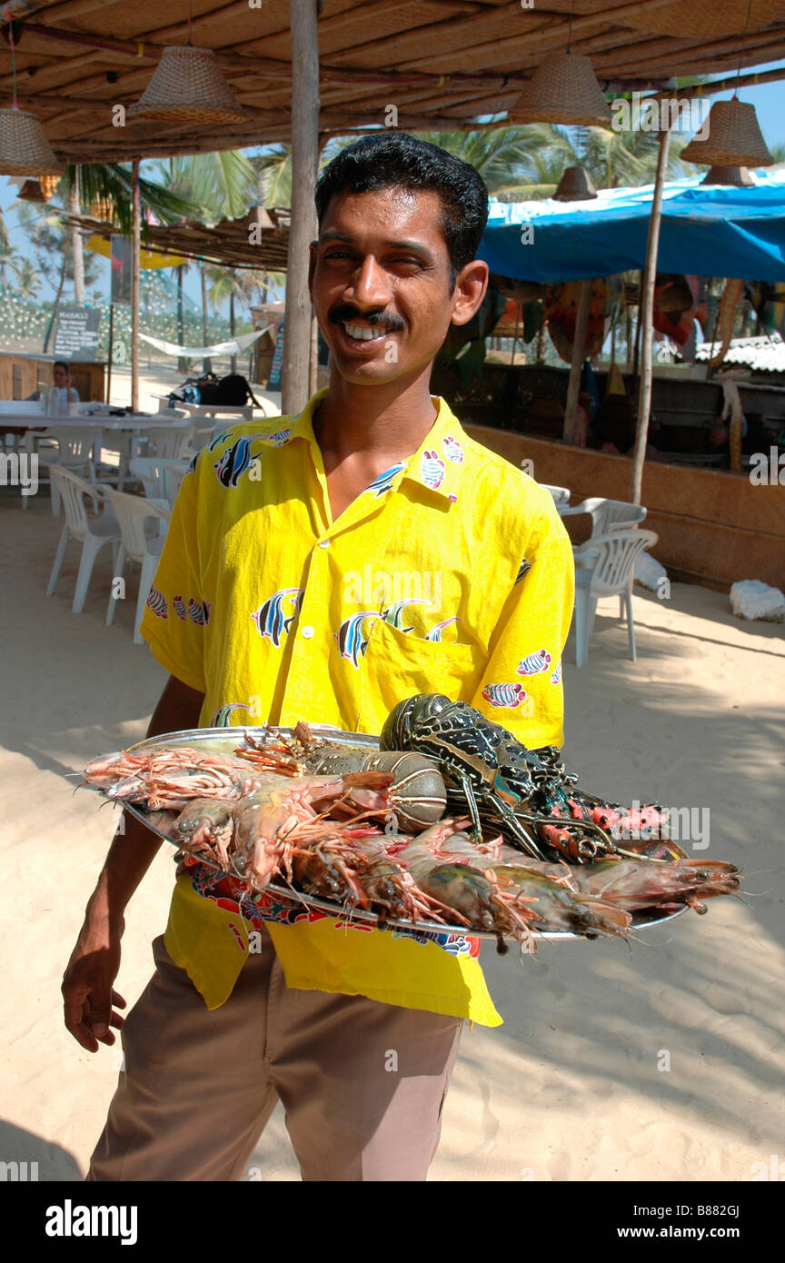 Local waiter holding a tray of lobsters at a beach cafe in Goa in India