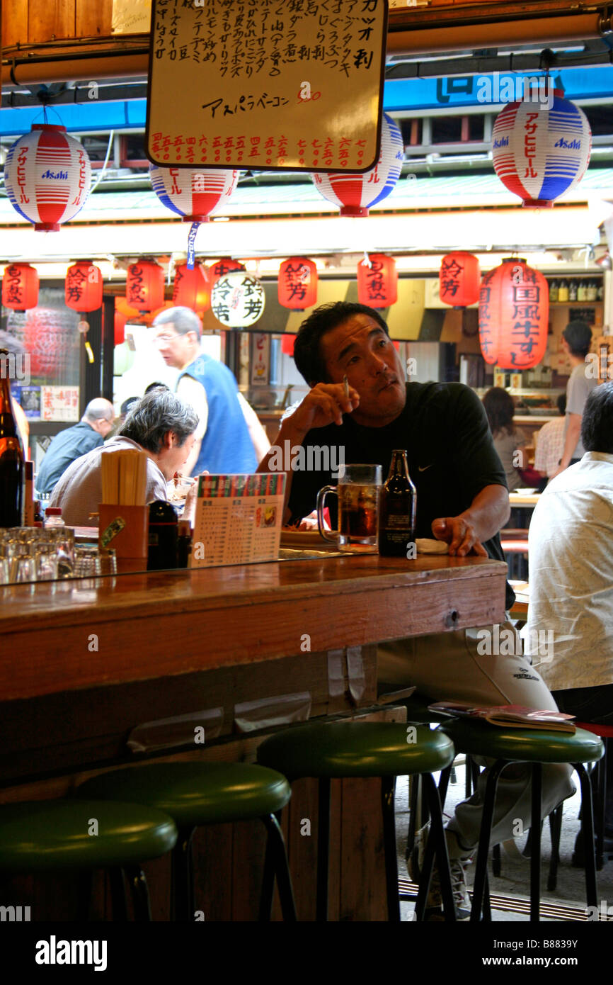 Japanese man sitting and drinking at an Izakaya bar, street in background, Tokyo Stock Photo