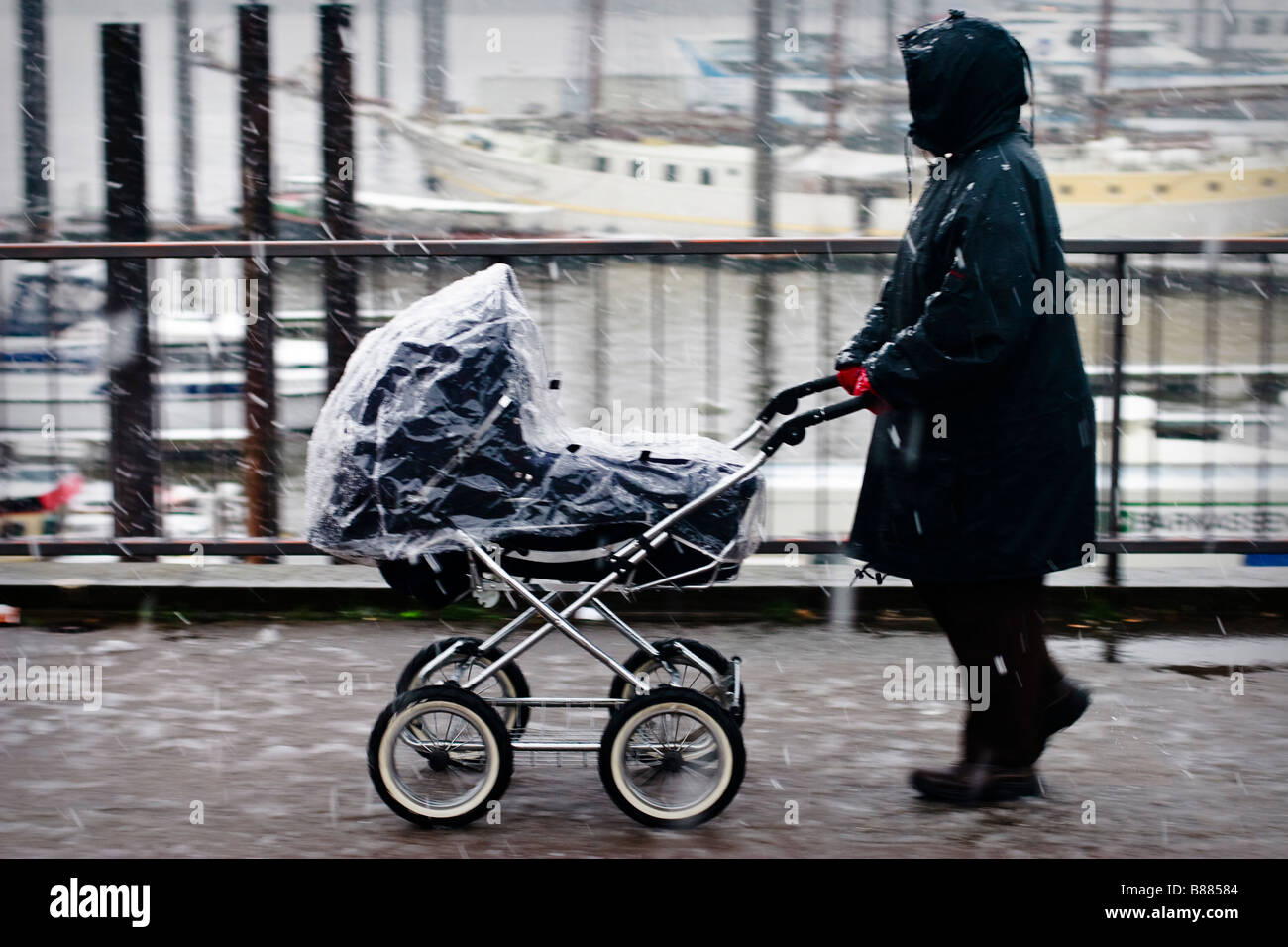 Woman in Rain jacket walks with a pram in snow covered Hamburg, Germany Stock Photo