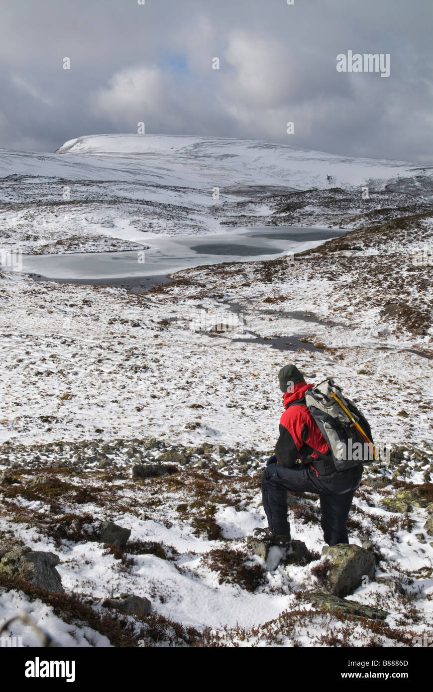 Hill walker looking towards an unnamed frozen loch and Carn a Gheoidh a munro at 975 metres