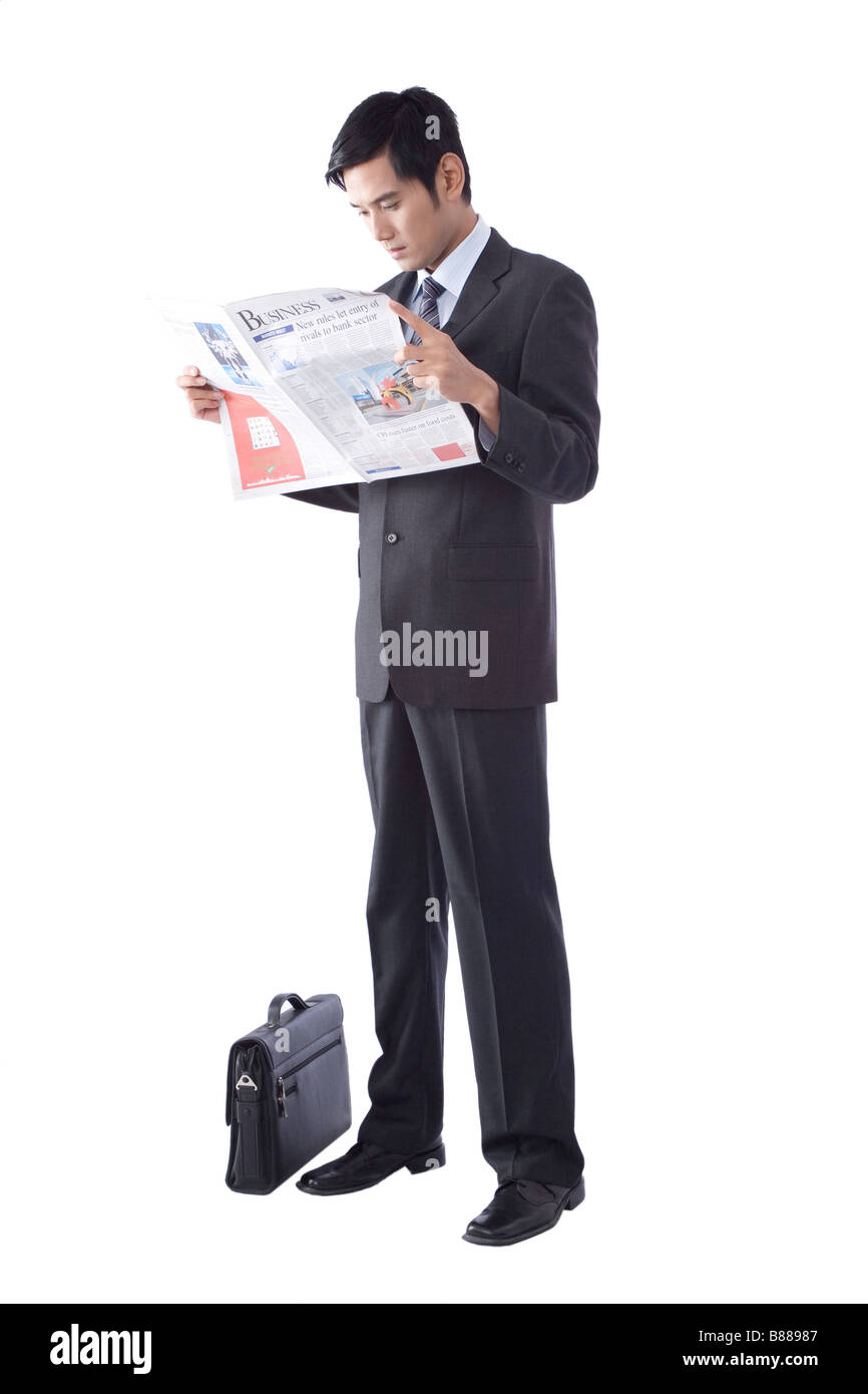 Young businessman reading newspaper with briefcase aside Stock Photo ...