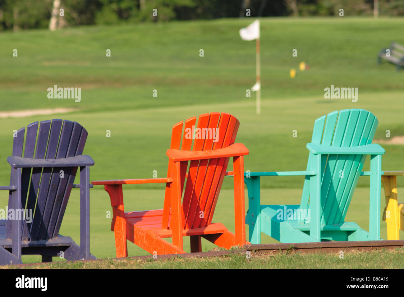 brightly colored wooden adirondack chairs beside a golf course Stock Photo Alamy
