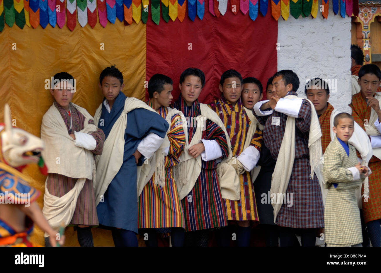 Young Bhutanese men in national dress, gho, watching masked dancers in the courtyard of Mongar Dzong during the Mongar festival Stock Photo
