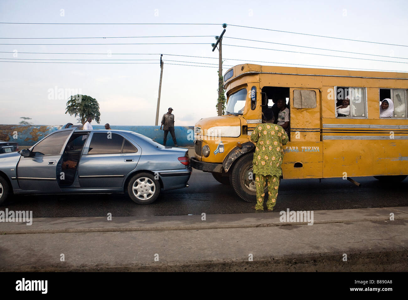 A yellow Nigerian bus has crashed into a private car whose driver is in discussion with the bus driver Stock Photo