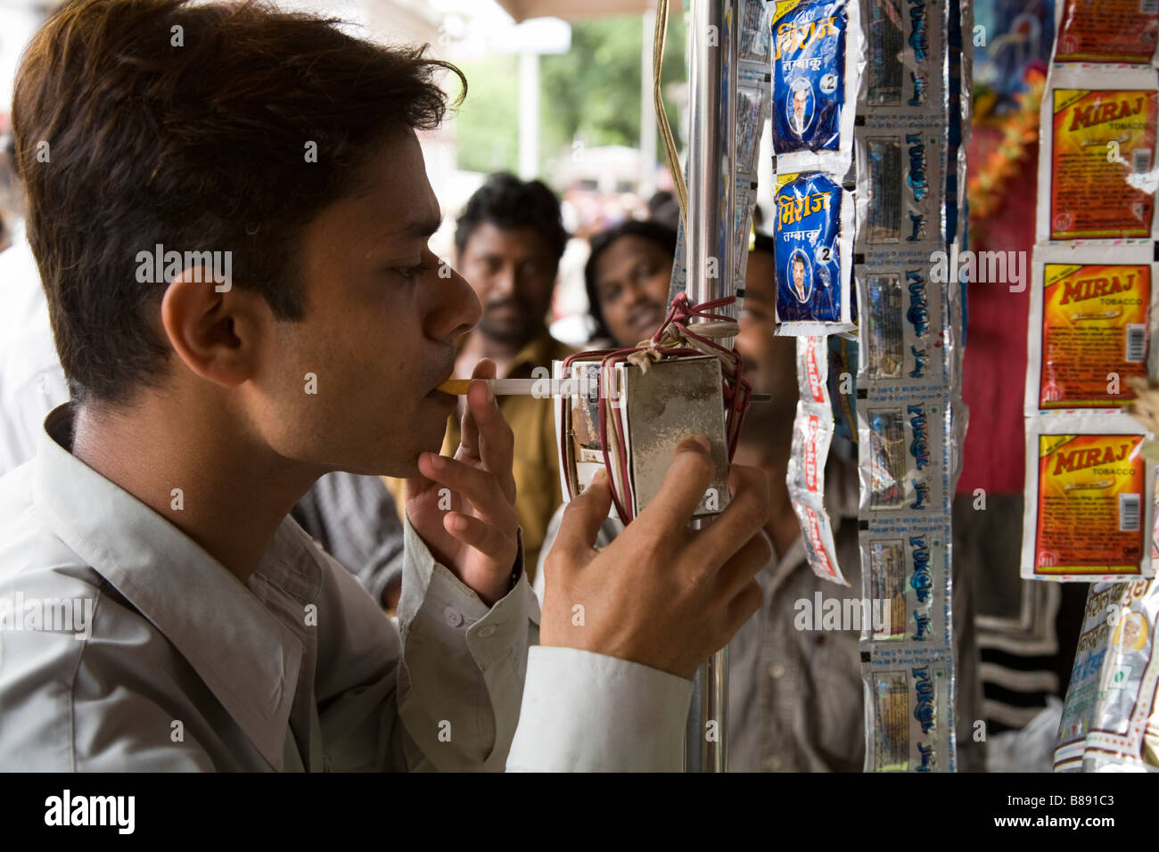 Indian man lights a single cigarette he has just bought using a hot plate  at the tobacconist kiosk that sold it. Mumbai. India Stock Photo