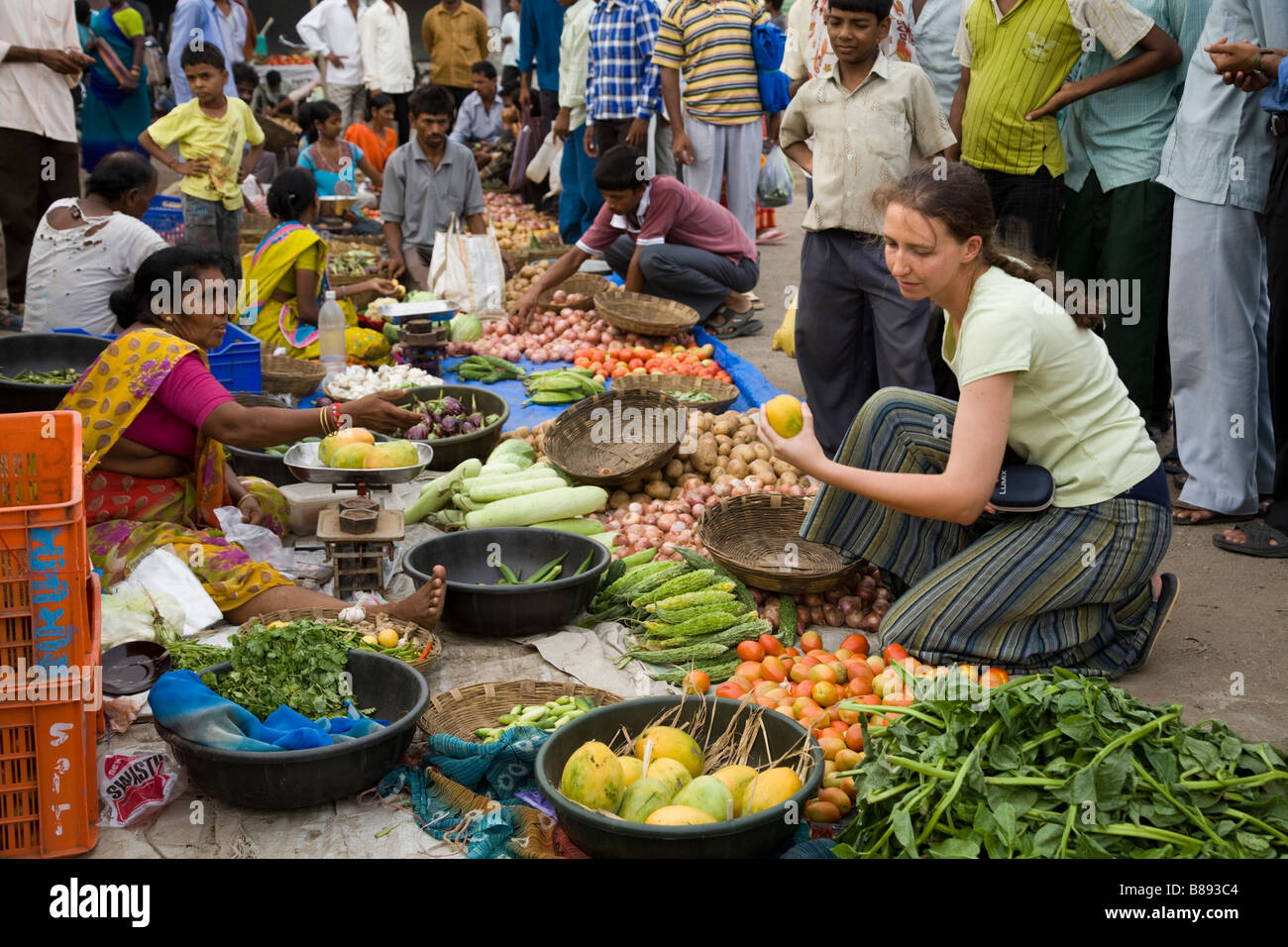 Western woman tourist choosing and buying fruit and vegetables / buys food at a local market stall. Hazira, Surat, Gujarat. India. Stock Photo