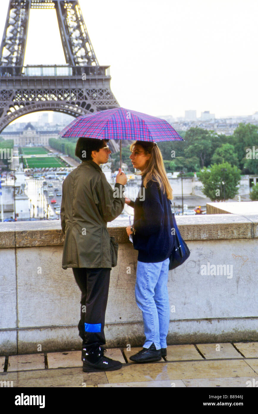 Young couple talk beneath umbrella by wall of the Trocadero with Eiffel Tower in distance paris france Stock Photo