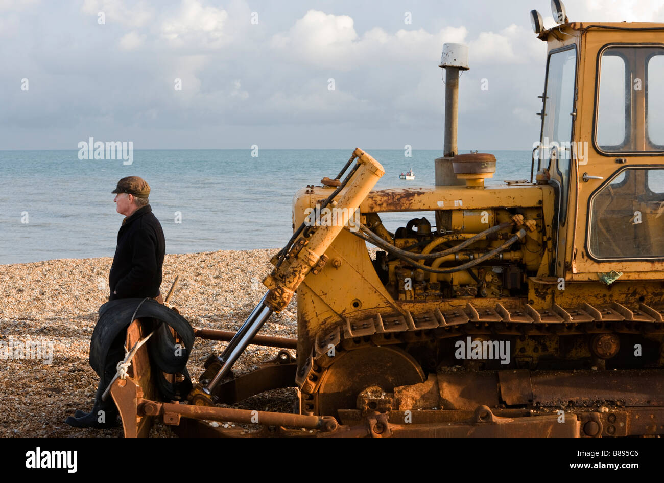 A man seated on heavy machinery a tracked vehicle on the shingle beach at Dungeness in Kent, UK. Stock Photo