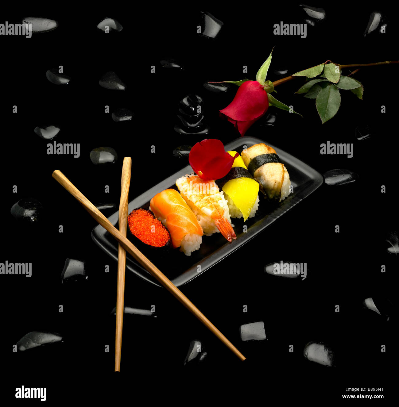 assorted sushi plate with a red rose on black pebbles over black background Stock Photo