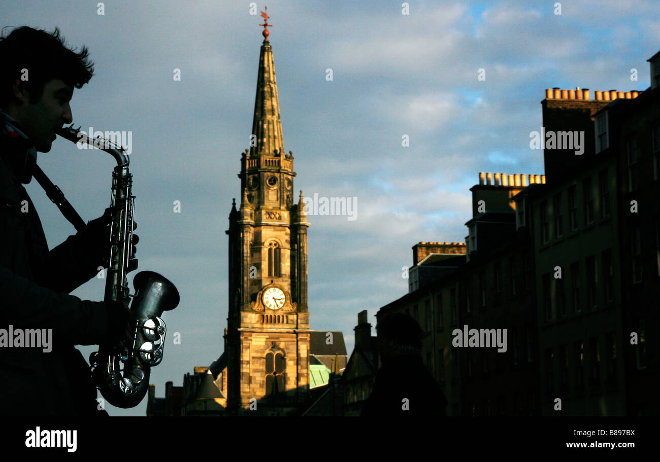 A silhouetted busker plays a saxophone on the Royal Mile near Tron Kirk in Edinburgh Scotland UK Stock Photo