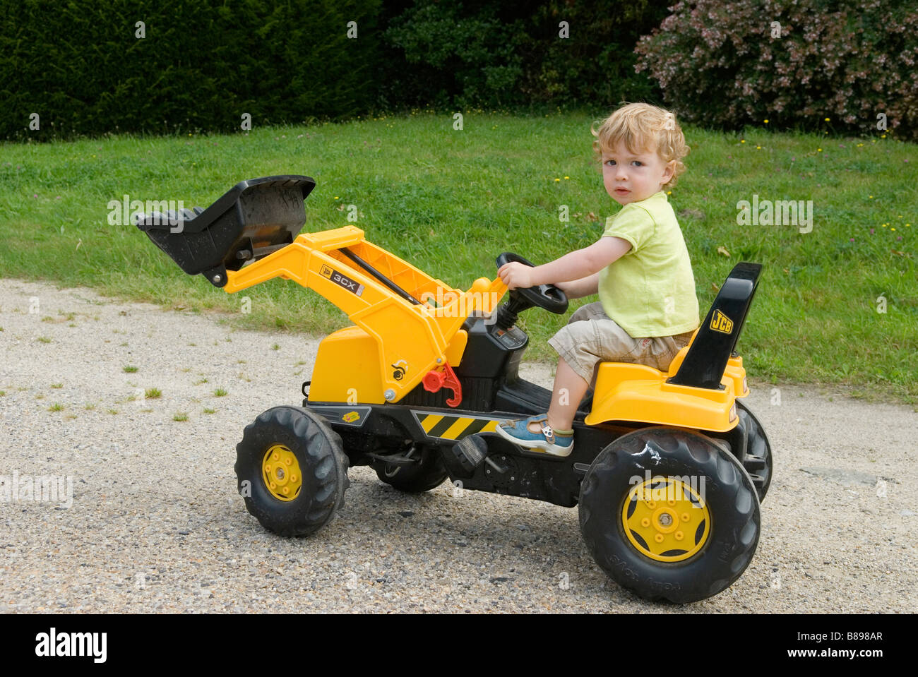 Young boy playing on yellow powered toy tractor Stock Photo