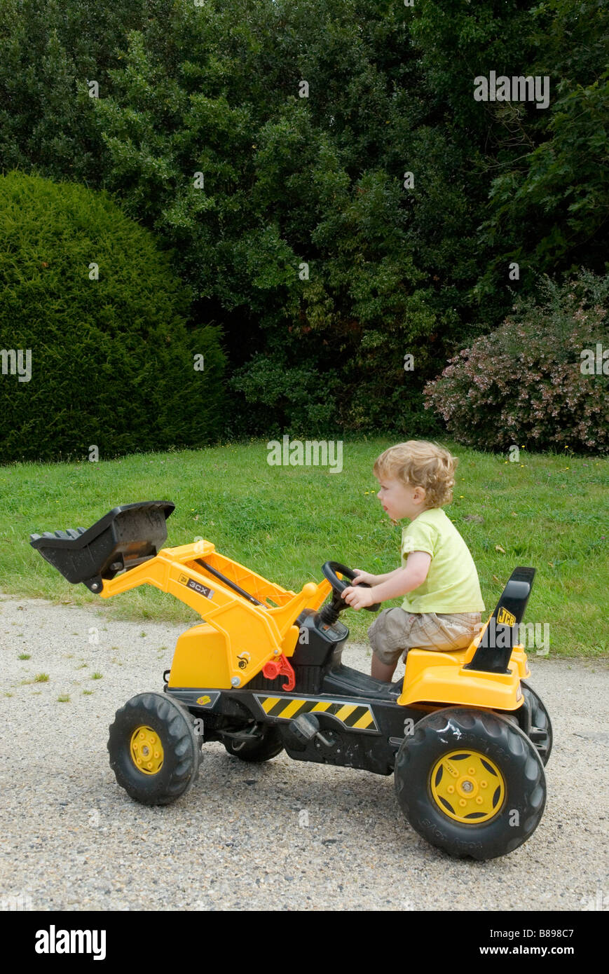 Young boy playing on yellow powered toy tractor Stock Photo