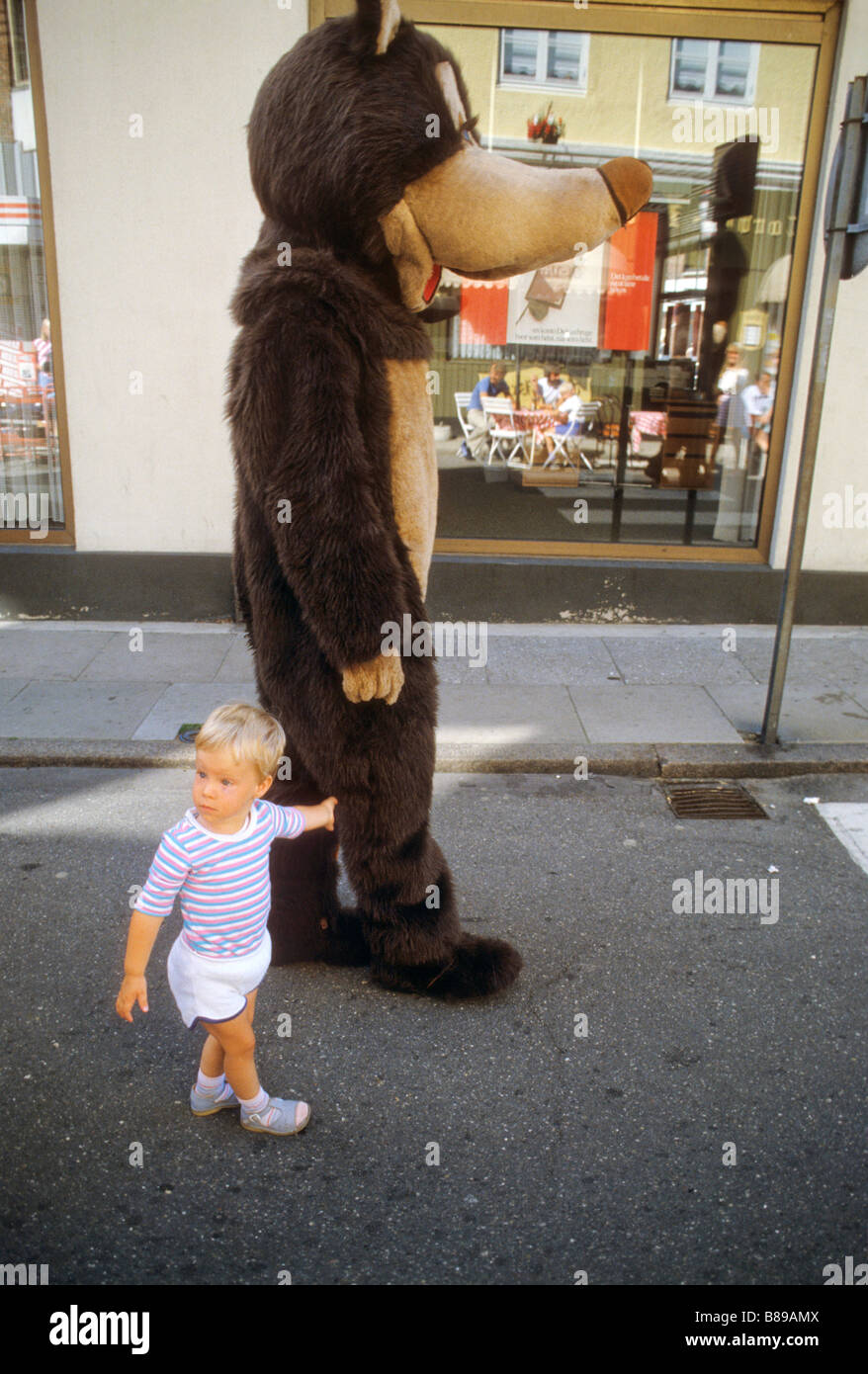 Small child holds hand of man dressed in bear suit in shopping area of town in Denmark Stock Photo