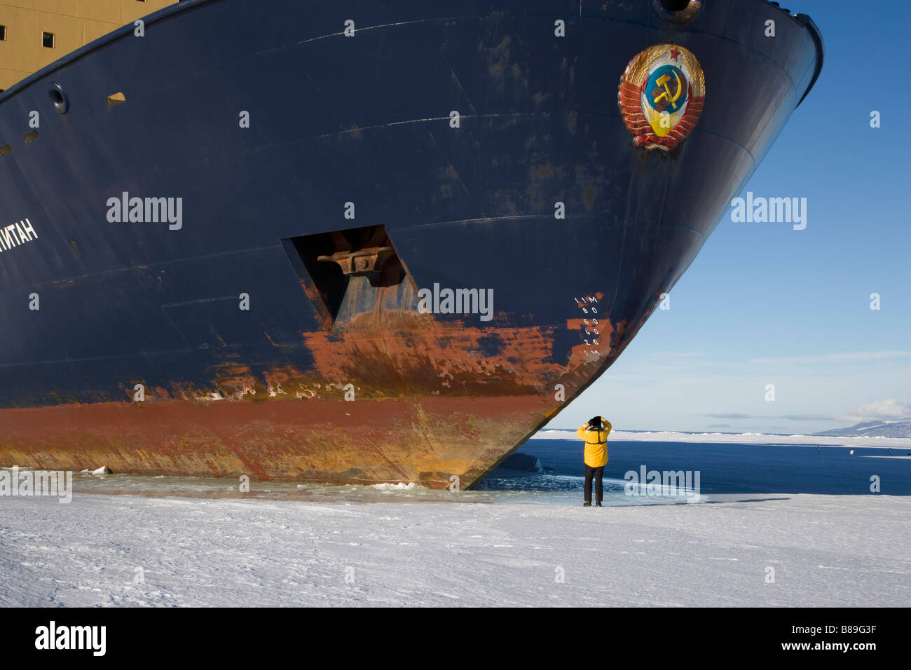 Photographer standing on ice taking a picture of the bow,  front hull of Russian Icebreaker ship parked in Ice in Antarctica blue sky snow Stock Photo