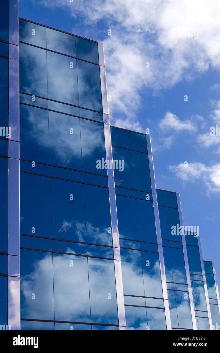 Five towers of a sleek modern glass office building with clouds and sky reflecting on the surface of the buildings Stock Photo