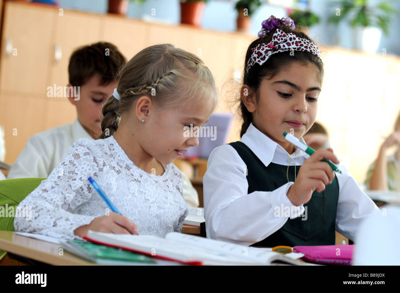 Two schoolgirls in a multicultural classroom. On the left a Christian Ukrainian girl, on the right a Muslim Tatar girl. Stock Photo