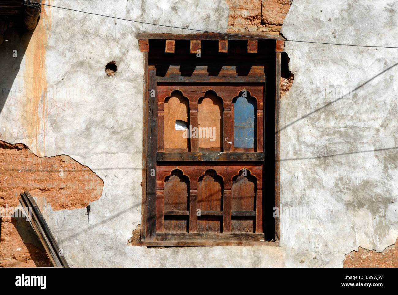 A traditional Bhutanese wooden windowframe boarded up in the plaster wall of a derelict building Stock Photo