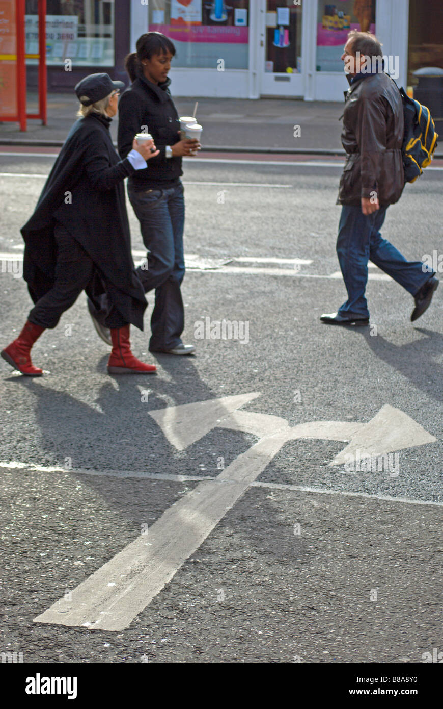three pedestrians crossing a road with road marking arrows pointing in