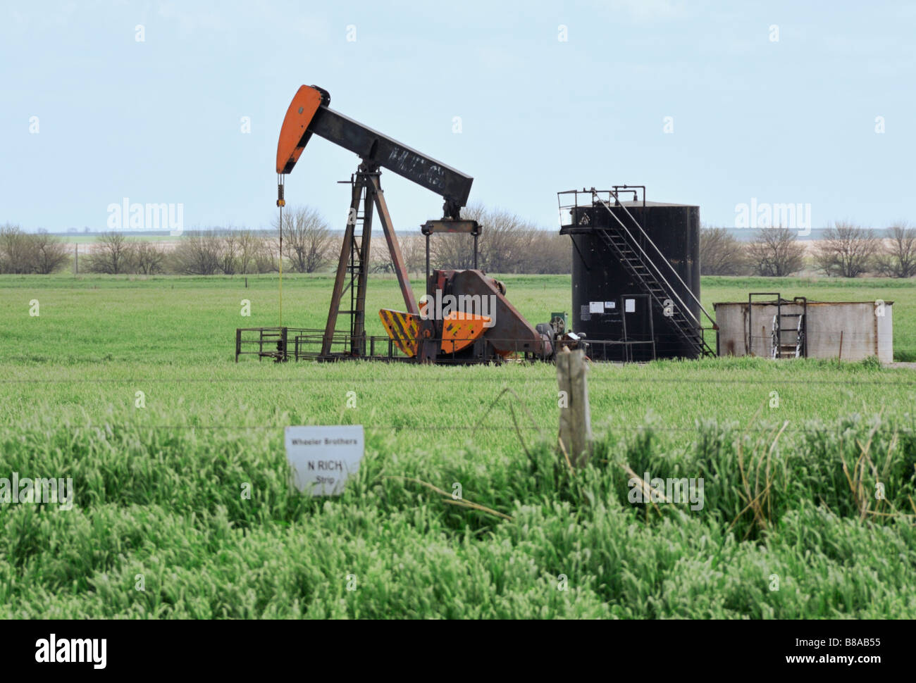 An oilfield pump jack in a field with storage tanks. Oklahoma, USA
