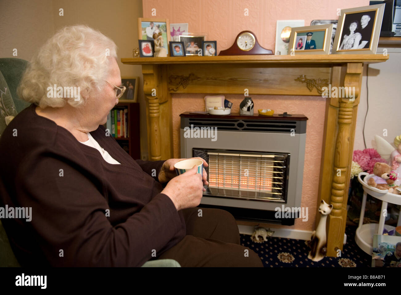 An elderly woman keeps warm in front of an electric fire in her UK home Stock Photo
