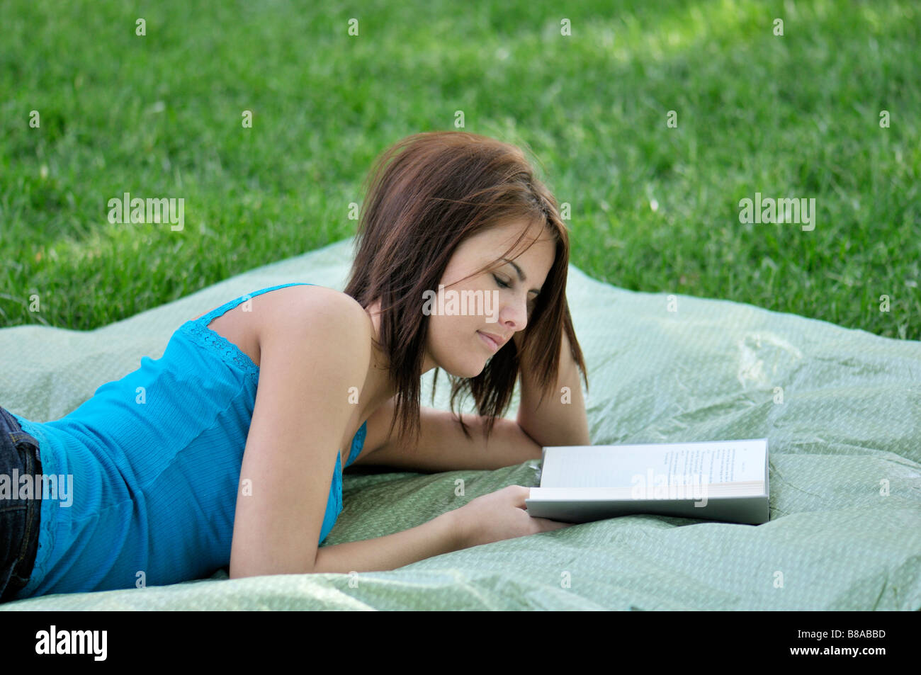 A pretty girl lies on a blanket outdoors and reads a book. USA. Stock Photo