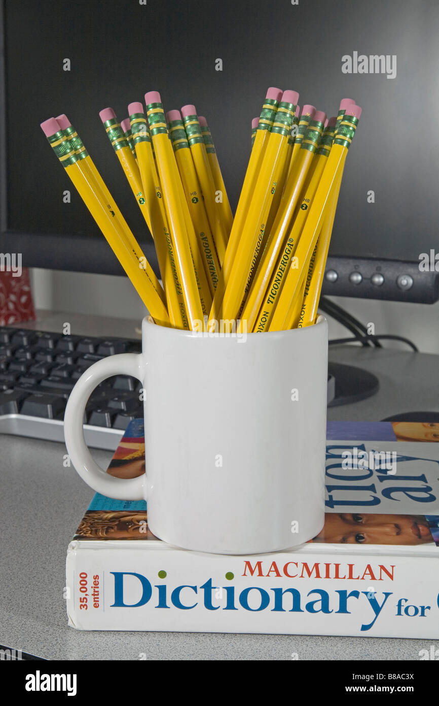 A cup or mug of number 2 Ticonderoga lead or graphite pencils and erasers in front of a computer and sitting on a dictionary Stock Photo