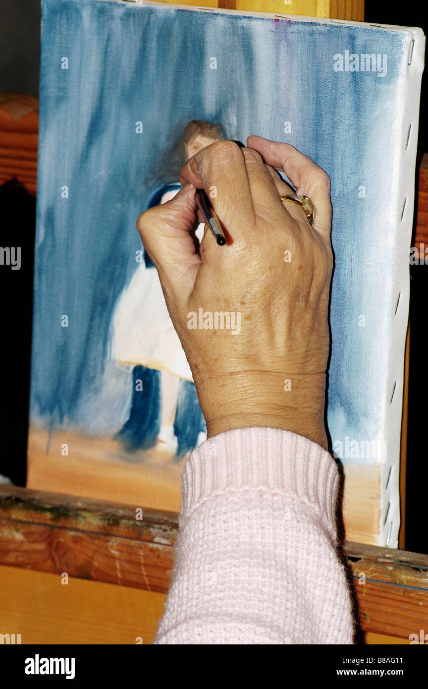an elderly womans hands painting a picture of a young woman in a studio setting Stock Photo