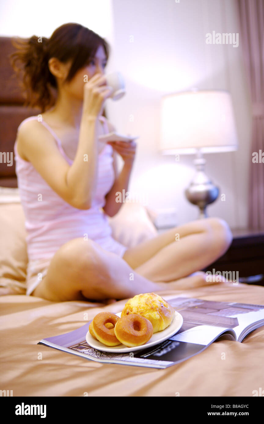 Young woman sitting on bed eating food Stock Photo Alamy