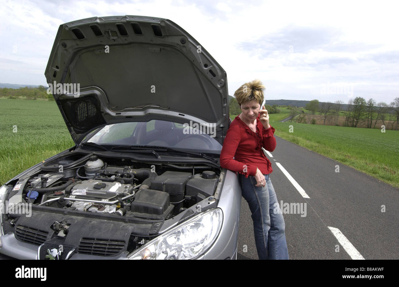 Car broken down with female driver alone phoning for help at the roadside Stock Photo