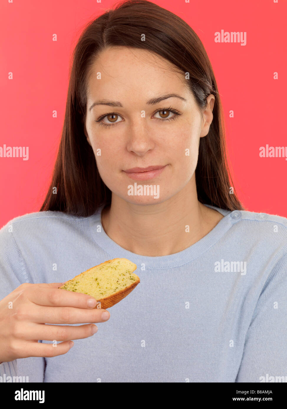 Young Woman Eating Freshly Cooked Italian Style Garlic Bread Against A Red Background With Her