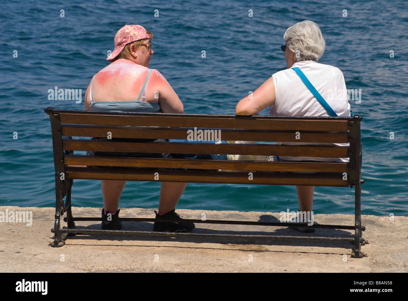 Hania / Chania, Crete, Greece. Sunburned woman with lotion on shoulders, sitting by the sea talking Stock Photo
